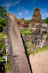 Carved stone stela lying against a wall with a temple in the background at My Son, Vietnam